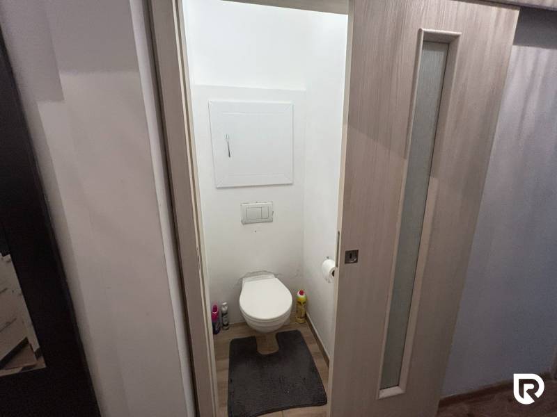 A toilet with a wooden decor floor in a studio apartment.