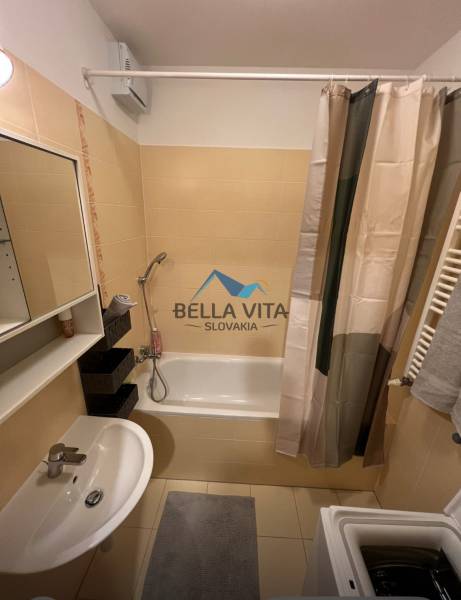 A bathroom in a 2-room apartment with a bathtub, sink, washing machine, and tiles.