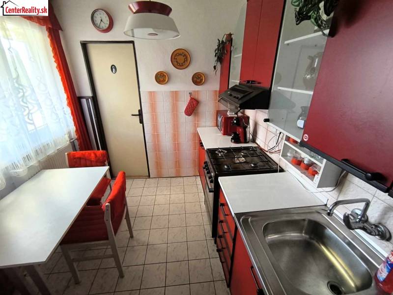 A kitchen in a family house with red cabinets, a dining table, and tiles.
