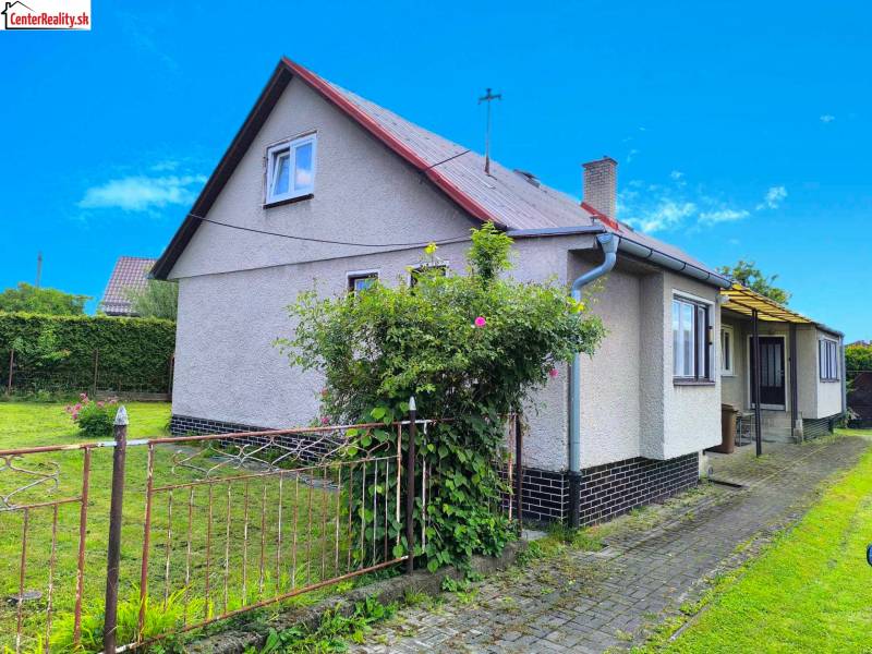 A family house in Nováky with a lawn and garden, surrounded by a fence and plants.