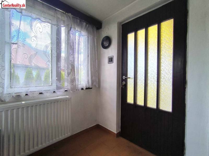 Interior of a family house with a window, radiator, and wooden door with glass inserts.