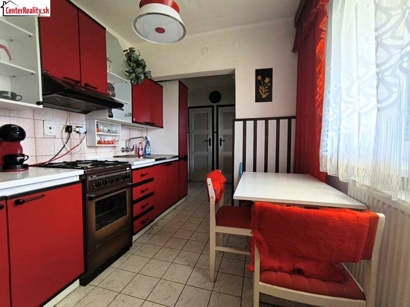 A kitchen in a family house. Red cabinets, dining table, curtains, coffee maker.