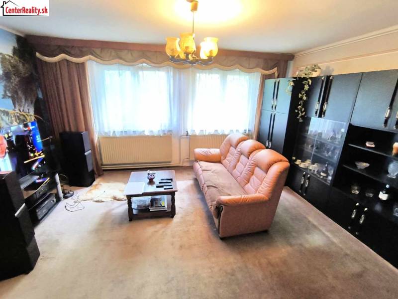 Living room in a family house with a brown sofa, cabinets, and a television on the wall.