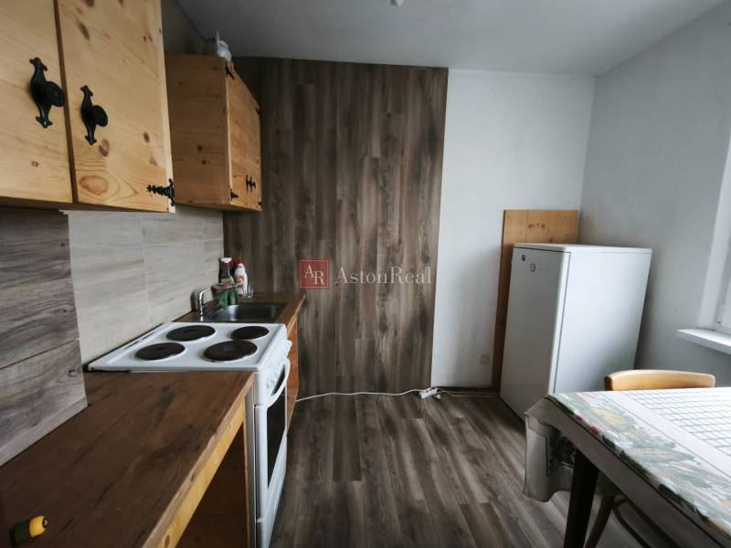 The kitchen in a studio apartment with a wood-patterned floor, wooden cabinets, table.