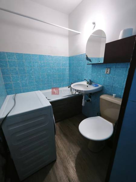 Bathroom with a bathtub, sink, toilet, and washing machine in a studio apartment. Floor with wooden decor.