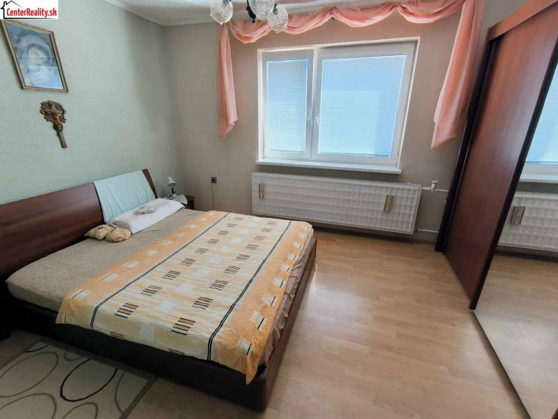 Bedroom in a family house with a bed, wardrobe, and wooden decor flooring.