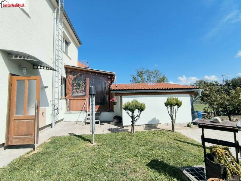 The exterior of a family house in Partizánske with a veranda and a garden under a blue sky.