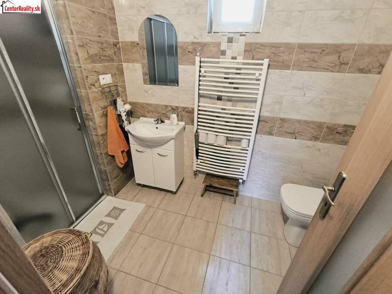 Bathroom with toilet in a family house with a shower, tiles, and a storage basket.