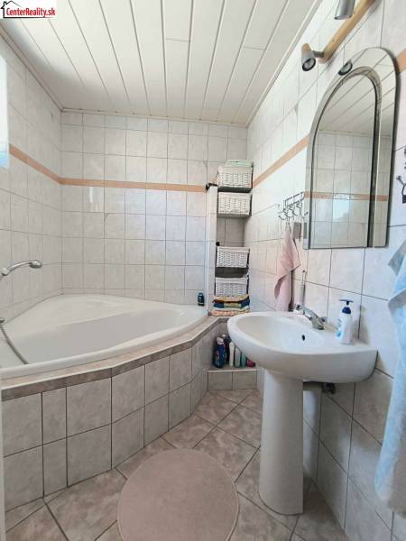 Bathroom in a family house with a corner bathtub, white tiles, and storage baskets.