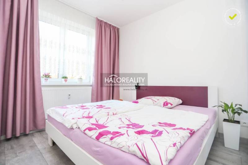 A bedroom in a two-room apartment with pink curtains and colorful bed linens.