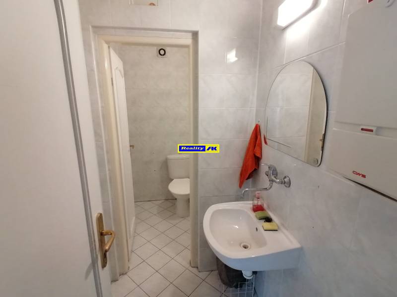 Bathroom in offices with a mirror, sink, and toilet on white tiles.