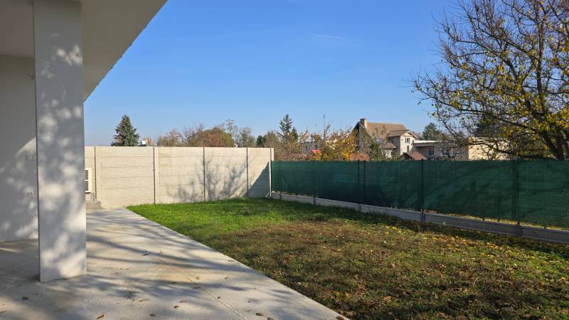 A garden of a family house in Piešťany with a lawn, concrete terrace, and fencing.