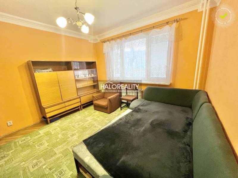 Living room in a 4-room apartment with orange walls, a green sofa, and a cabinet.