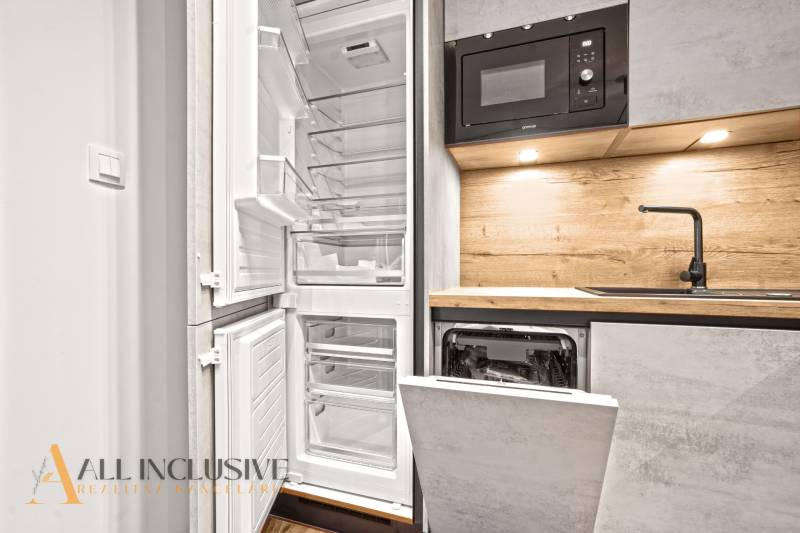 A kitchen in a 2-room apartment with an open refrigerator and a built-in dishwasher.