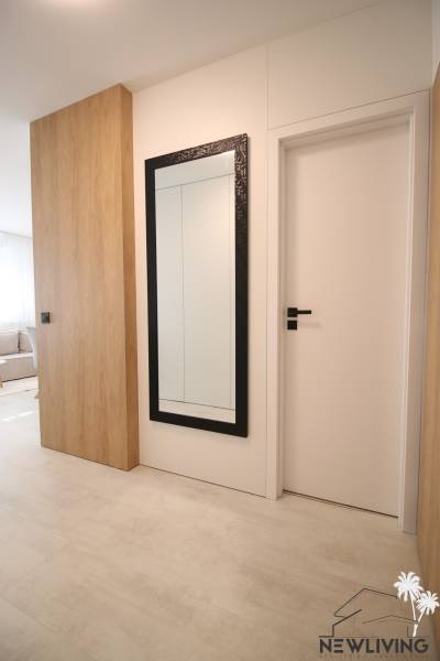In a one-room apartment, there is a mirror with a black frame and a floor with a wood decor.