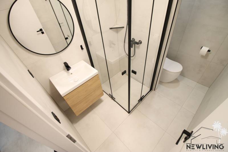 Bathroom in a studio apartment with a large mirror and a shower, tiled floor.