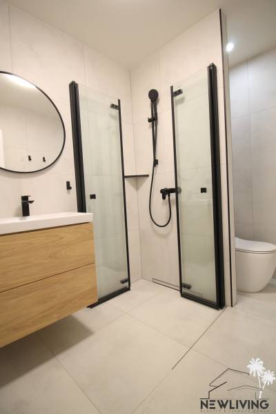 Bathroom in a studio apartment with storage space, shower, and round mirror.
