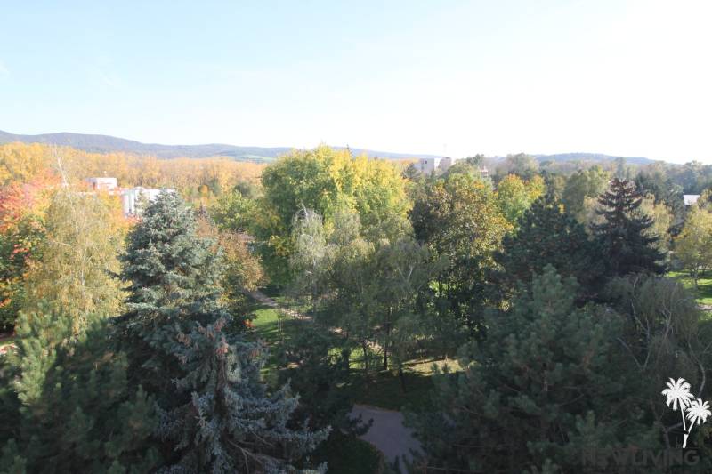 View from Valová Street in Piešťany with dense greenery and gentle hills in the background.