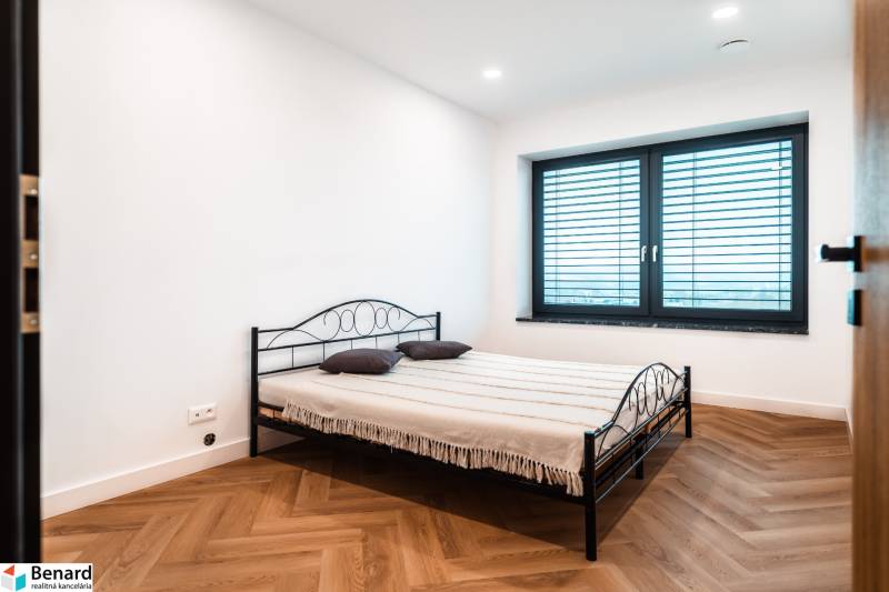 A bedroom in a family house with a metal bed, white walls, and a wooden decor floor.