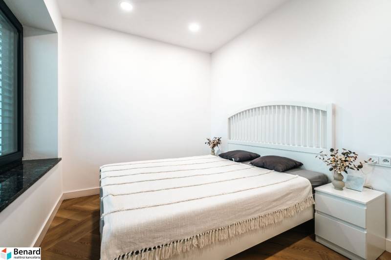 A bedroom in a family house with a wood-patterned floor, white walls, and a bed.