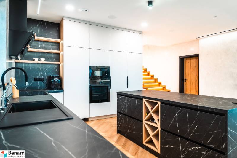 A kitchen in a family house with dark countertops and a wooden decor floor.