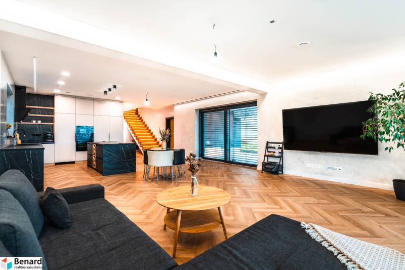 Living room in a family house with a kitchen, stairs, TV, and a wooden decor floor.
