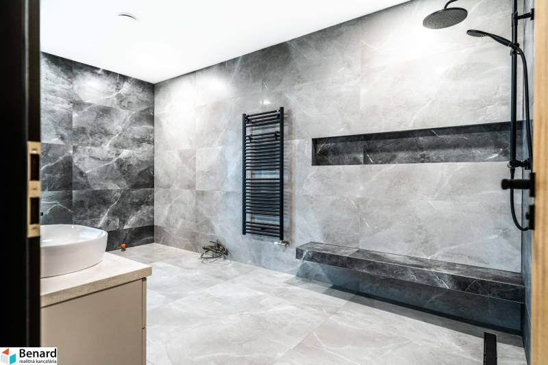 A bathroom in a family house with a black shower enclosure and gray wall tiles.