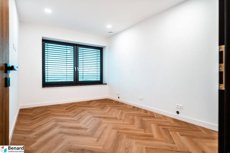 A room in a family house with a wooden decor floor, white walls, and a large window.