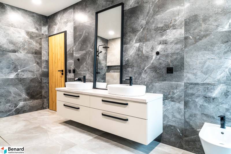 A bathroom with double sinks and dark gray tiles in a family house.