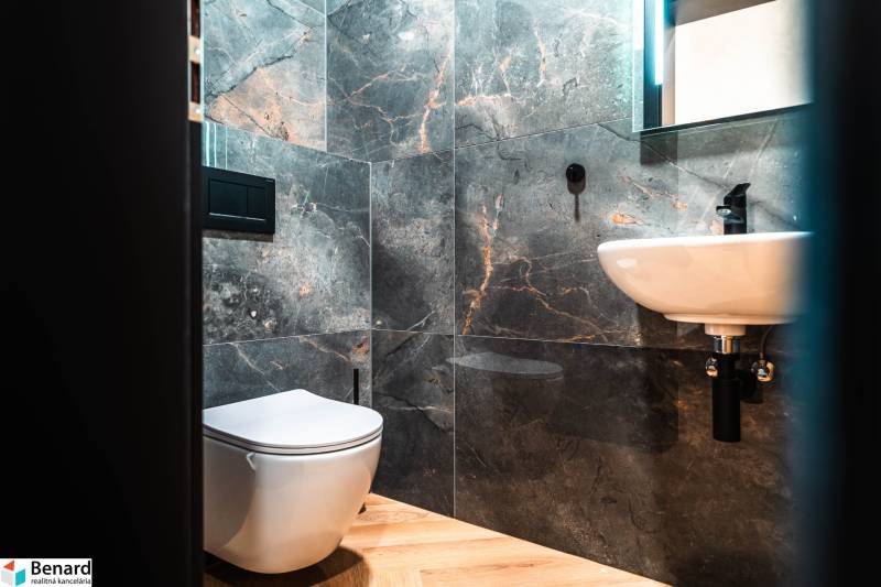 A bathroom in a family house with dark tiles and a wooden decor floor.