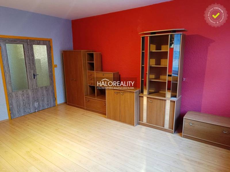 A room in a 3-room apartment with a wooden decor floor and a red wall.