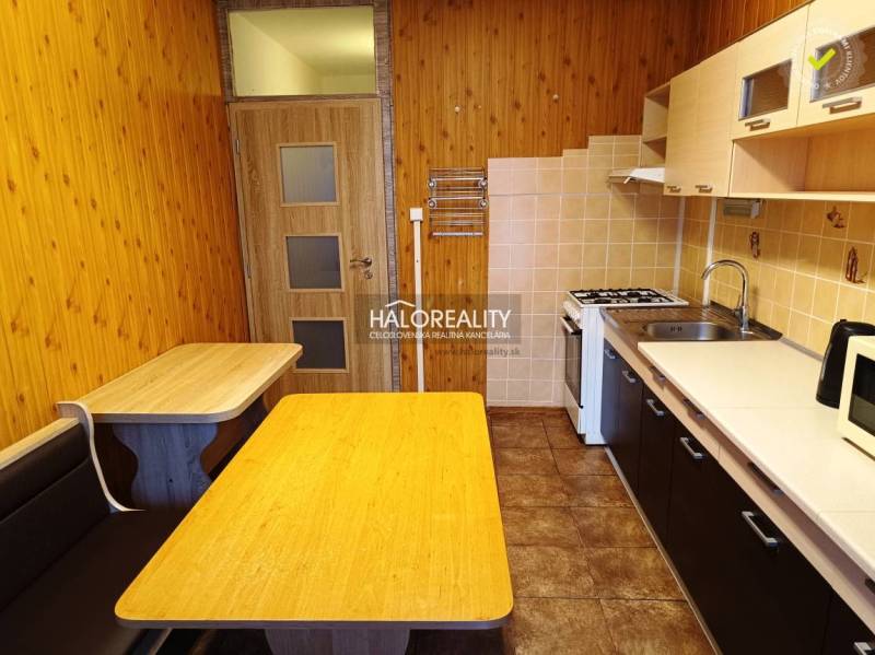 A kitchen in a 3-room apartment with a wood-patterned floor, a table, and a built-in bench.