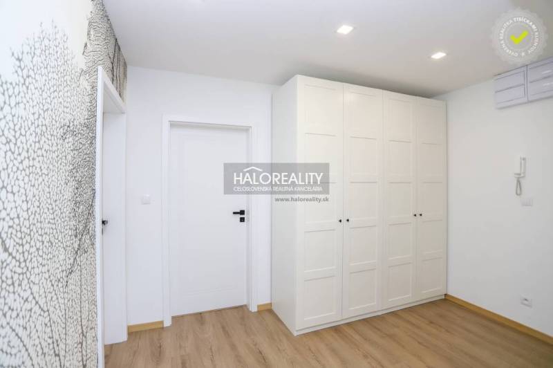 White wardrobe with wood-patterned flooring in a 2-room apartment, subtle patterned wall.