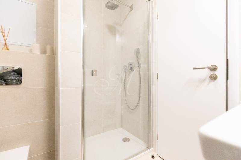 A bathroom with a glass shower enclosure and light tiles in a studio apartment.