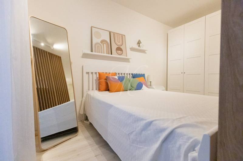 Bedroom in a studio apartment with a bed, colorful pillows, a mirror, and a large wardrobe.