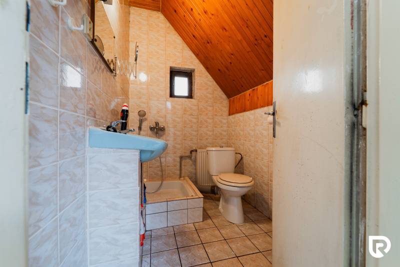 Bathroom with toilet and shower in a family house, tiled floor, wooden ceiling.