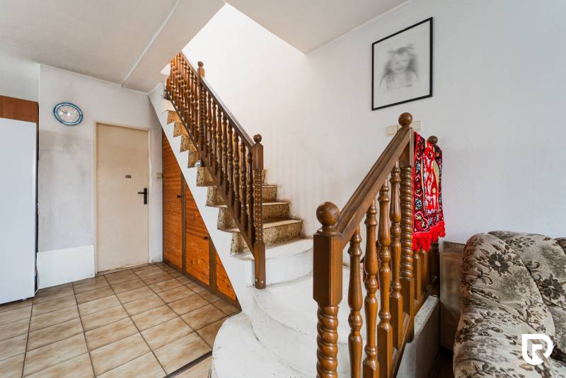 Interior of a family house with a staircase, deep red carpet, and a painting on the wall.