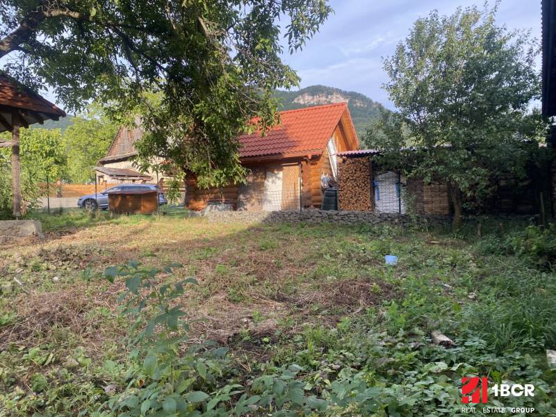 A cottage in Zliechov with a red roof, surrounded by greenery and wood on the property.
