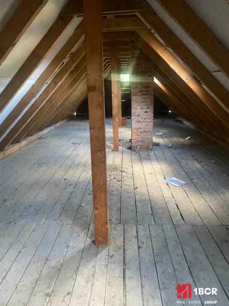 Attic in a cottage with wooden beams and a brick chimney, floor with wooden decor.