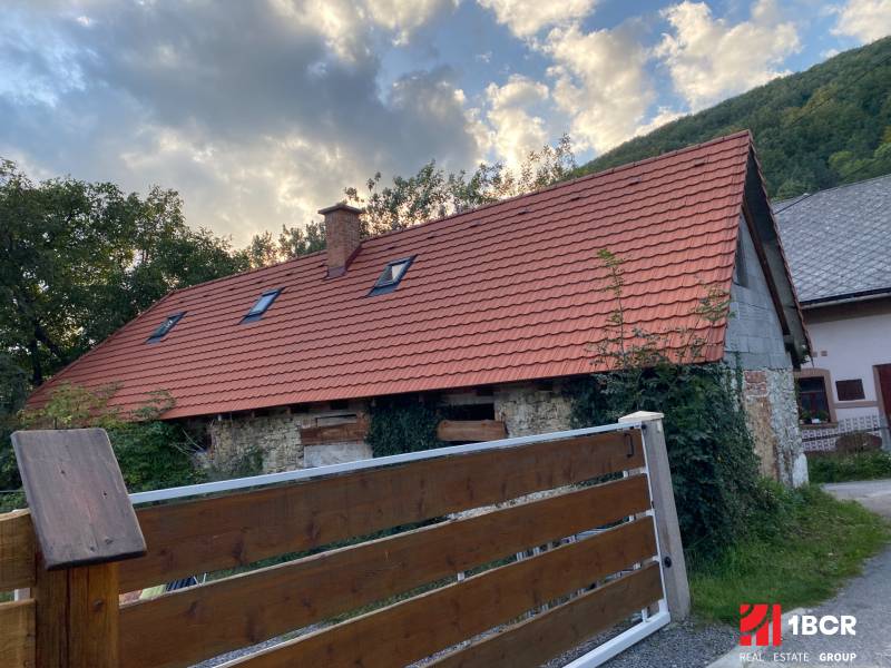 A cottage in Zliechov with a red roof and a wooden fence against the backdrop of mountains.