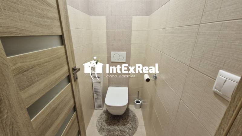 A toilet in a 3-room apartment with wood-decor tiles and flooring.