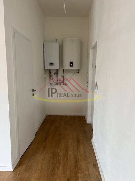 A narrow hallway in a 2-room apartment with a wood-patterned floor and a boiler on the wall.