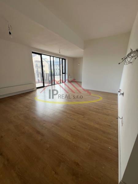 Spacious living room in a two-room apartment with wood-patterned flooring and a large window.