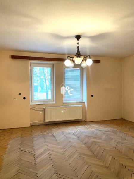 A room in a two-room apartment with a wooden decor floor and a hanging chandelier.