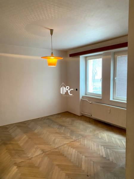 A room in a 2-room apartment with a wood-decor floor and a window with blinds.
