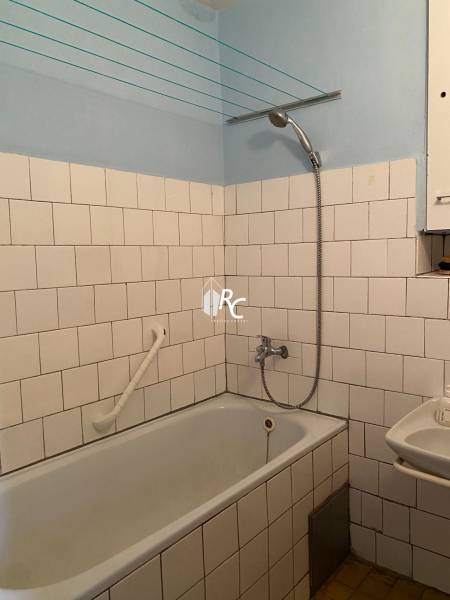 Bathroom in a 2-room apartment with a bathtub, white tiles, and a showerhead.