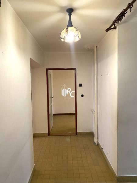 A hallway with tiles and a chandelier leading to a room in a 2-bedroom apartment.