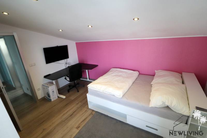 A room in a family house with a wooden decor floor, a bed, and a black table.