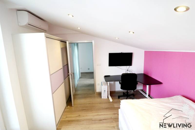 A room in a family house with a wooden decor floor, a work desk, and air conditioning.