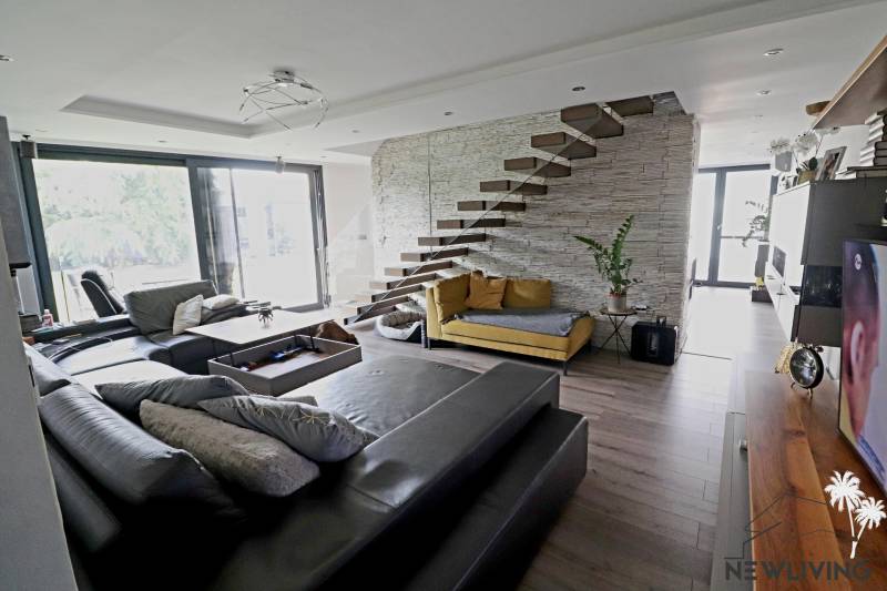 Living room with a comfortable sofa, open staircase, and large windows, designed on Jánošíkova Street.